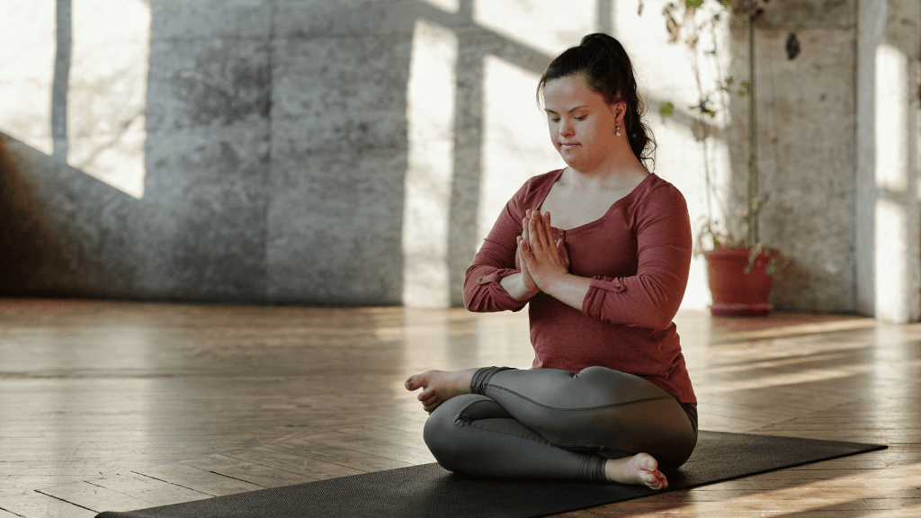 A young woman with Down syndrome meditates in a yoga pose