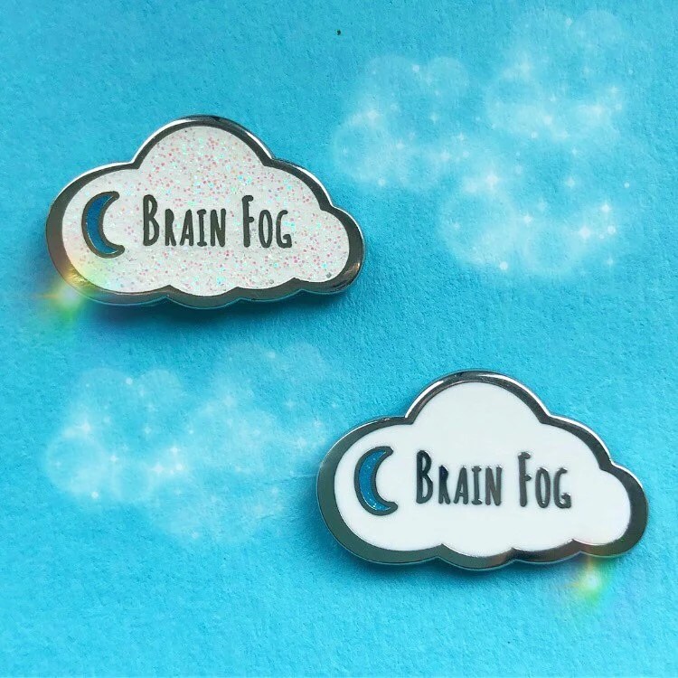 Two cloud-shaped pins with a moon symbol and the words "Brain Fog." One pin is glittery and one is not.